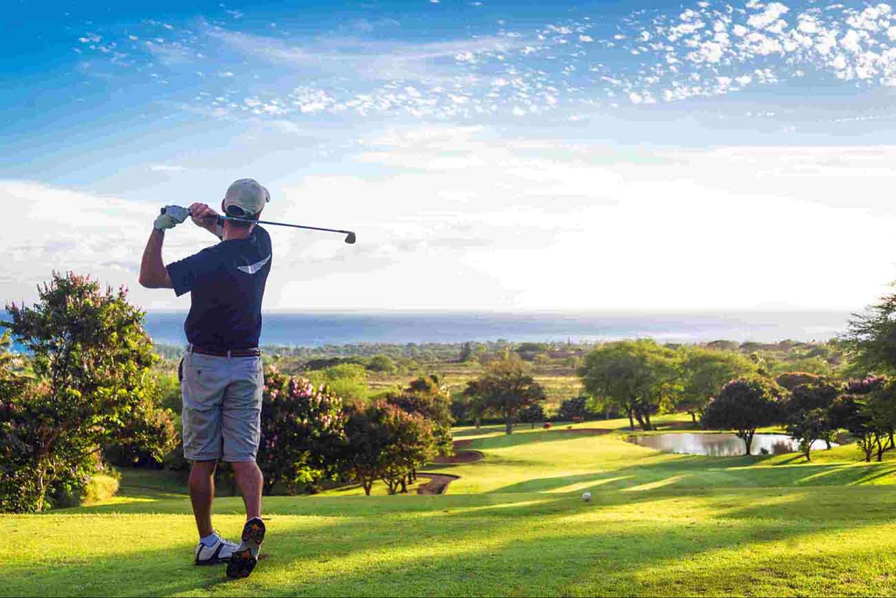 golfer teeing off on a beautiful hole with a view of the ocean in the distance