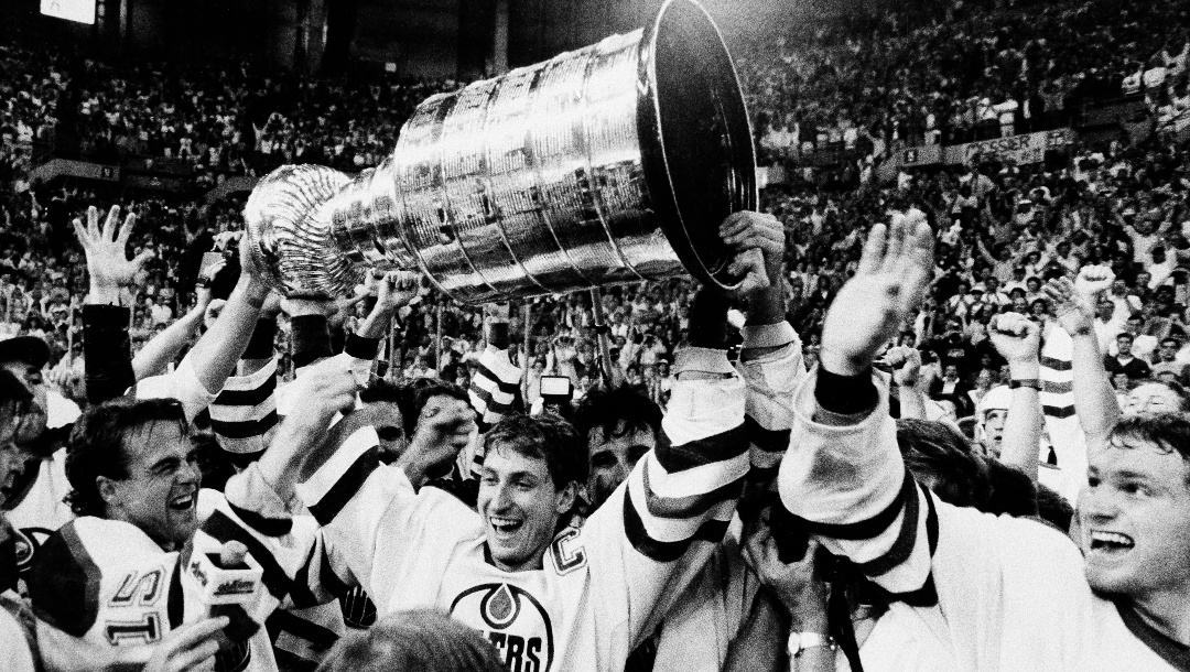 Edmonton Oilers team caption Wayne Gretzky is flanked by teammates as he skates with the Stanley Cup following their 3-1 victory over the Philadelphia Flyers in the seventh game of the Stanley Cup finals in Edmonton on May, 31, 1987. From left are Kent Nilsson, Gretzky and at far right Marty McSorley. (AP Photo/Larry Macdougal)